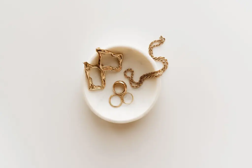 Anillos, pendientes y una cadena de oro en un cuenco blanco
